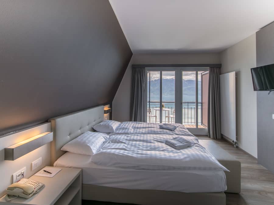 Ein modernes Hotelzimmer mit einem großen Bett, einem Nachttischtelefon und Blick auf die Berge durch das Fenster.