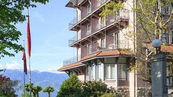 A multi-story hotel with balconies, a stone facade, and a view of mountains.