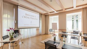 A spacious conference room with a large screen displaying "Bienvenue à l'hôtel Prealpina" and a modern, well-lit interior with wooden floors and contemporary furniture.