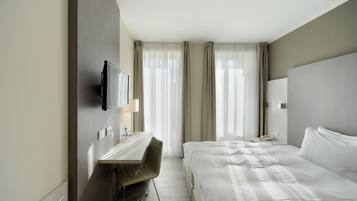 A hotel room with a bed, a desk with a chair, a television, and a window with curtains.