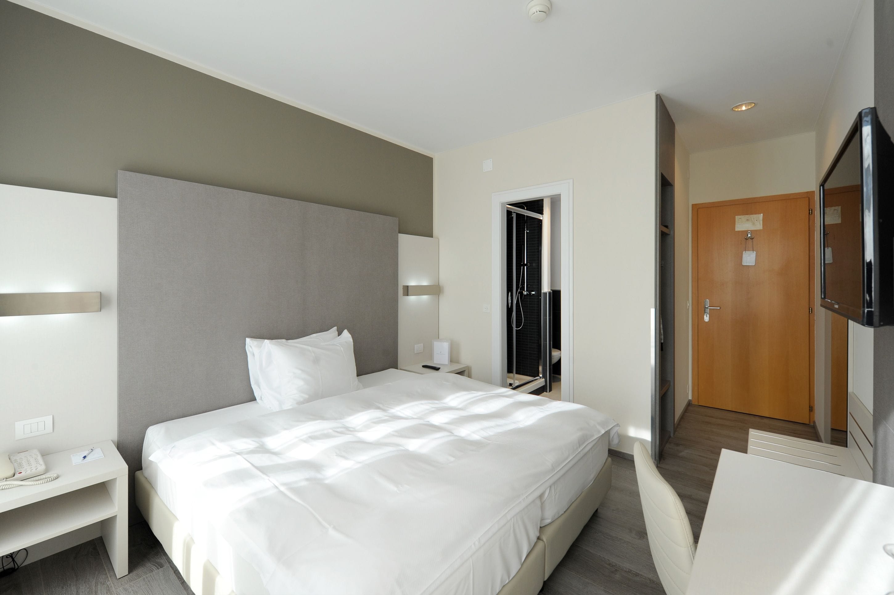 A modern hotel room with a large bed, bedside table, and a television.
