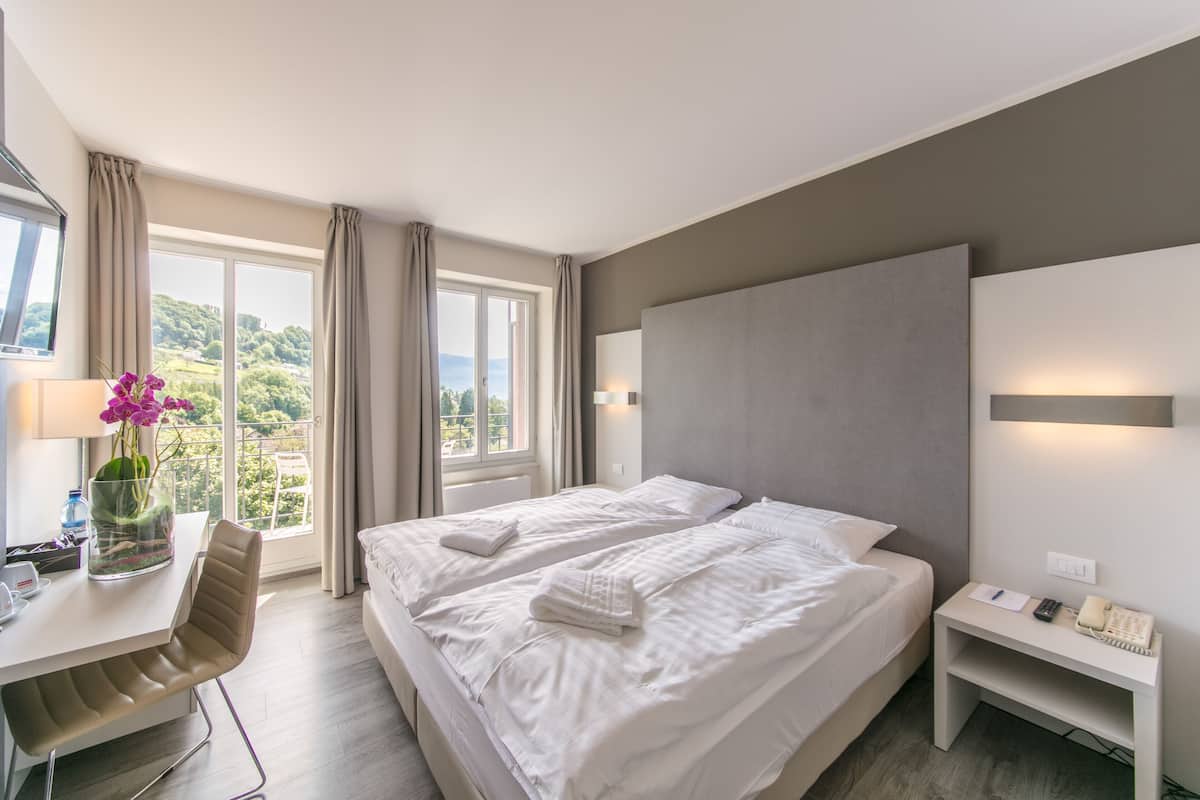 A hotel room with two beds, a desk, a chair, a nightstand, and a view of the outdoors.