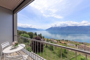 A balcony with a table and chairs, overlooking a lake with mountains in the background. - Hôtel Préalpina (Chexbres)
