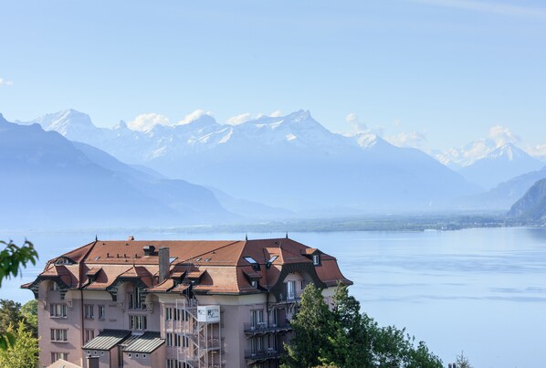 A hotel with a red-tiled roof, multiple balconies, and a view of snow-capped mountains across a lake. - Hôtel Préalpina (Chexbres)