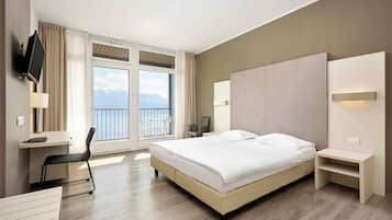 A hotel room with a large bed, a desk, a chair, a TV, and a view of the mountains.