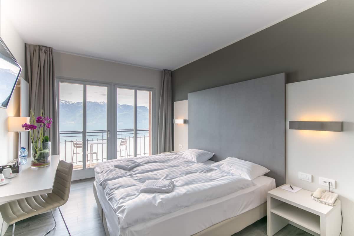 A hotel room with a large bed, a desk with a chair, a phone, and a view of the mountains through the window.