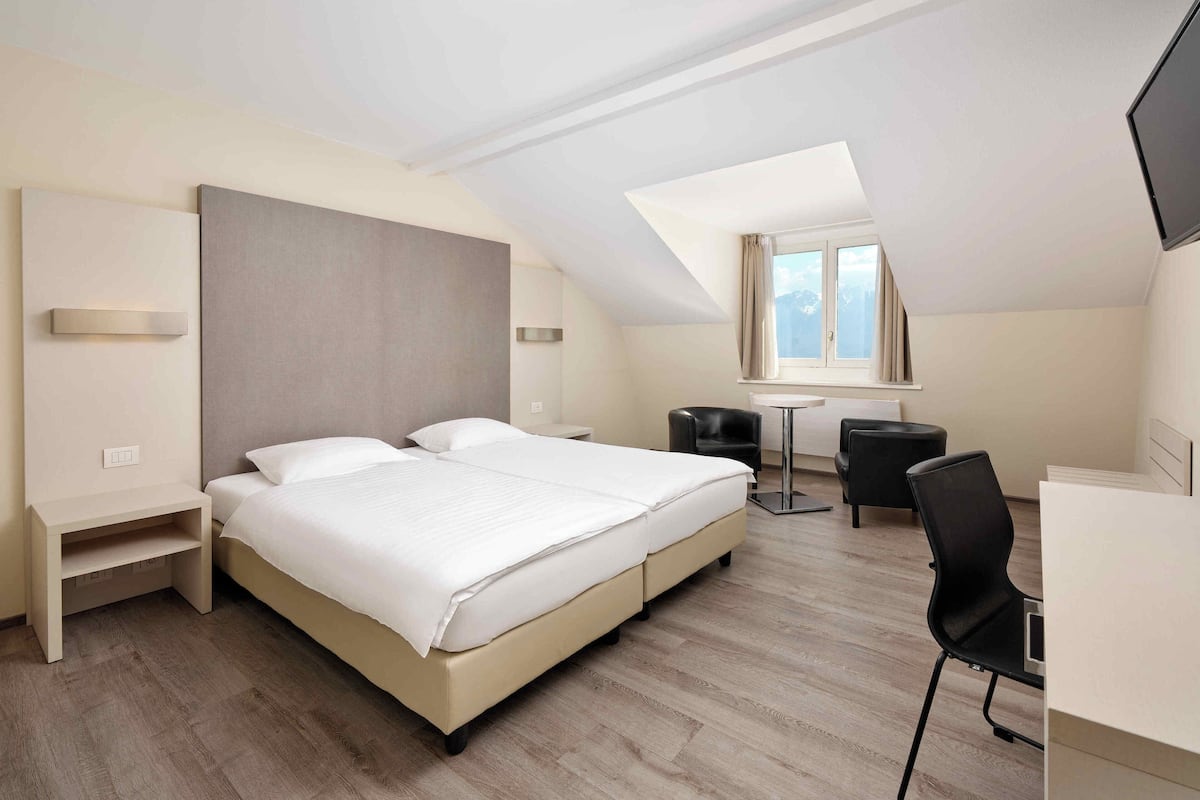 A modern hotel room with a large bed, a desk, two chairs, and a TV.