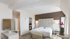 A modern hotel room with a large bed, a bedside table, a small desk, a chair, a mirror, and a vase with flowers. - Hôtel Préalpina (Chexbres)
