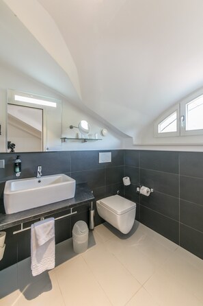 A modern bathroom with a large sink, toilet, and a mirror above the sink. - Hôtel Préalpina (Chexbres)