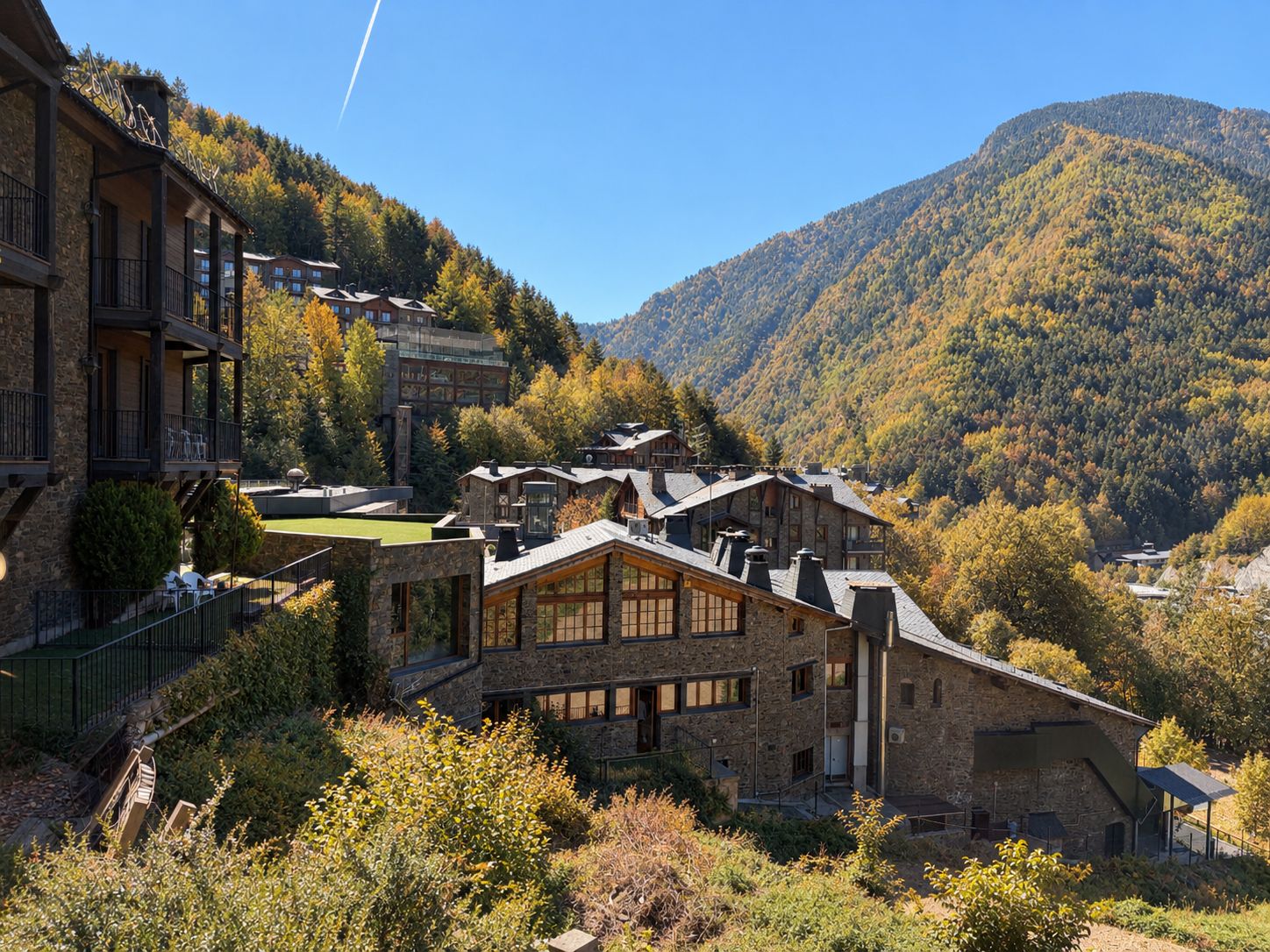 Et fjeldhotel med flere bygninger, en stenfasad og udsigt over den omkringliggende skov og bjerge.