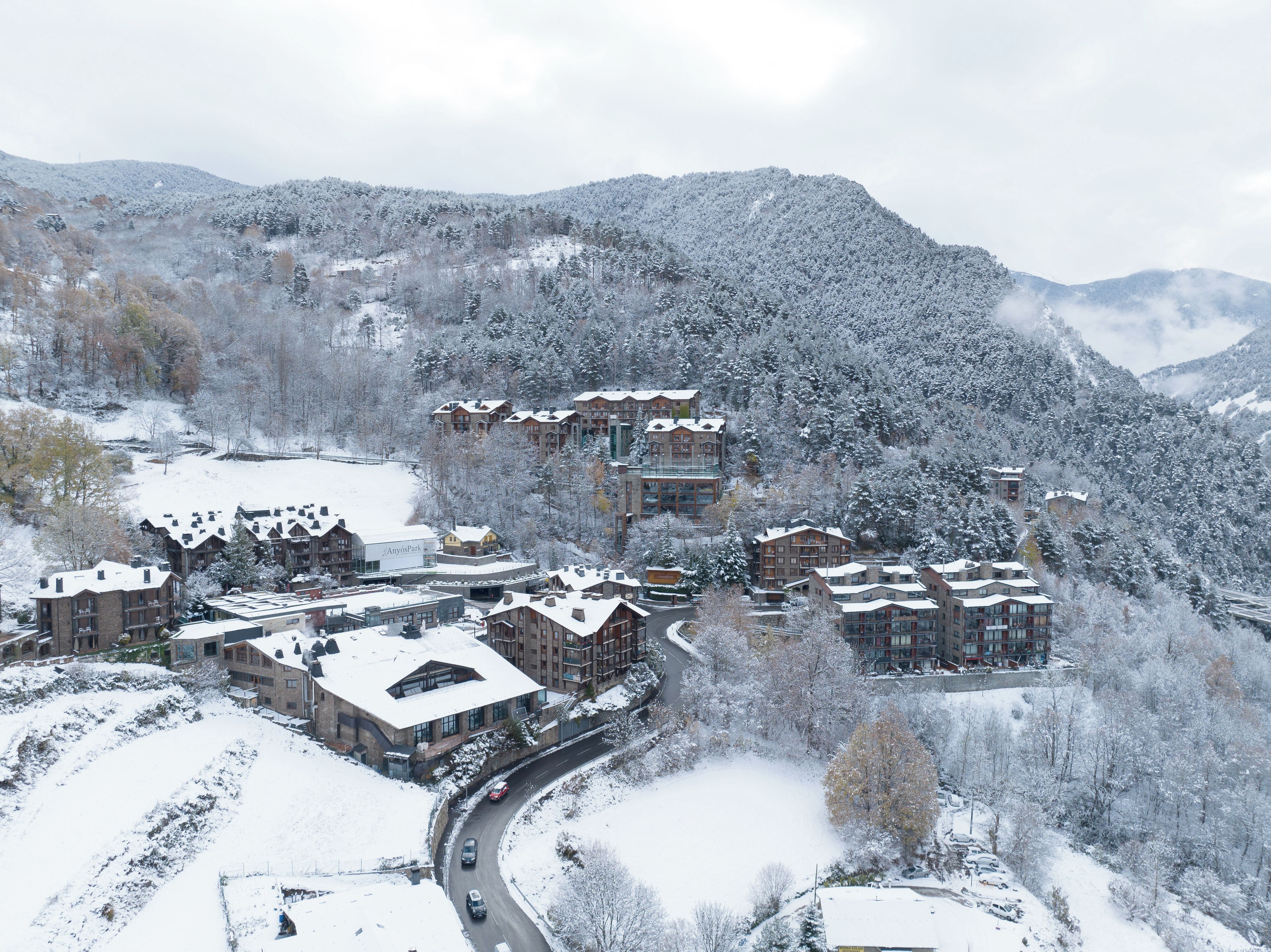 A snow-covered mountain resort with multiple buildings, a winding road, and a ski slope.