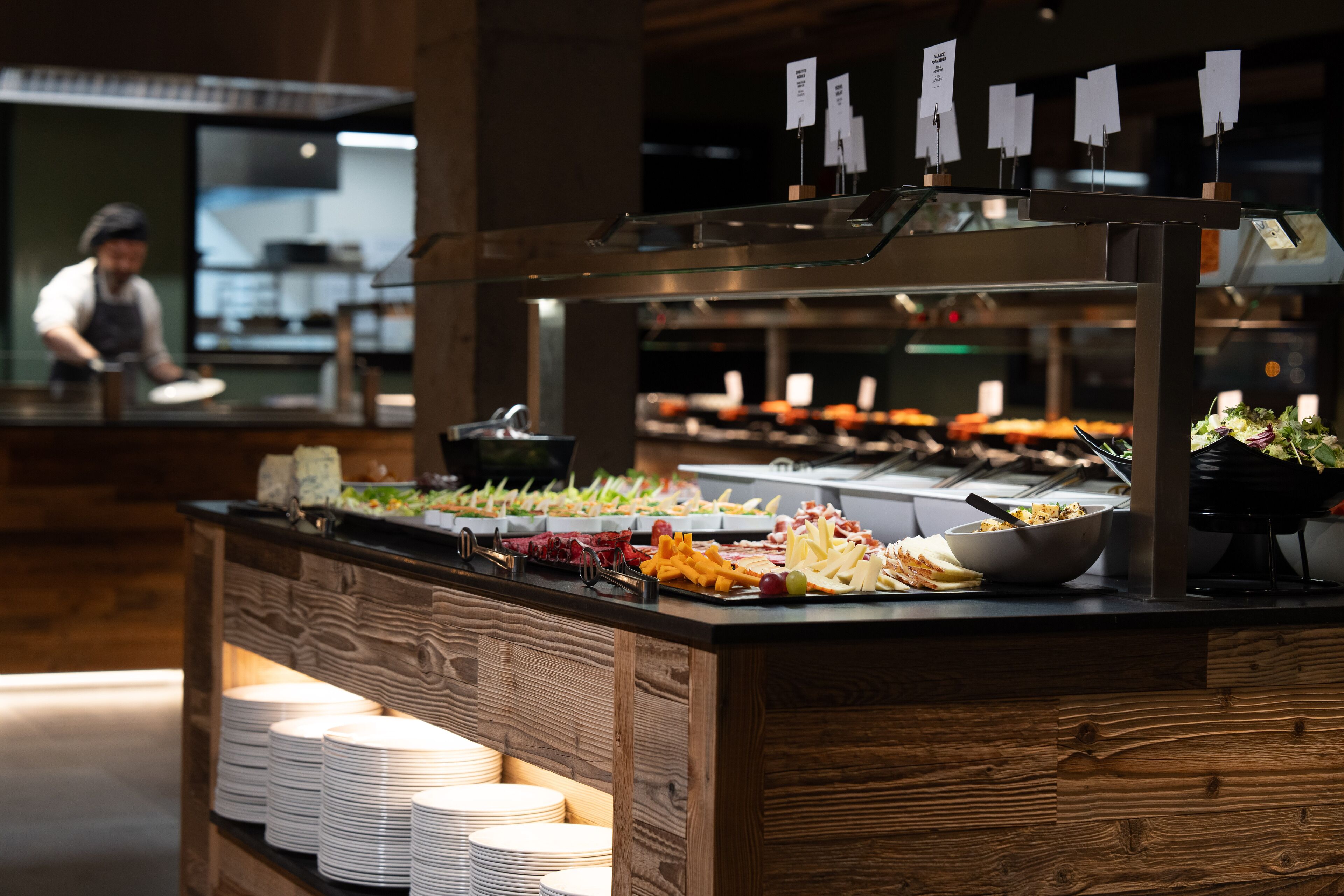 Uma área de buffet com diversos alimentos e uma pilha de pratos brancos.