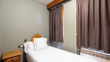 A bedroom with a bed, a wooden nightstand, a radiator, and brown curtains.