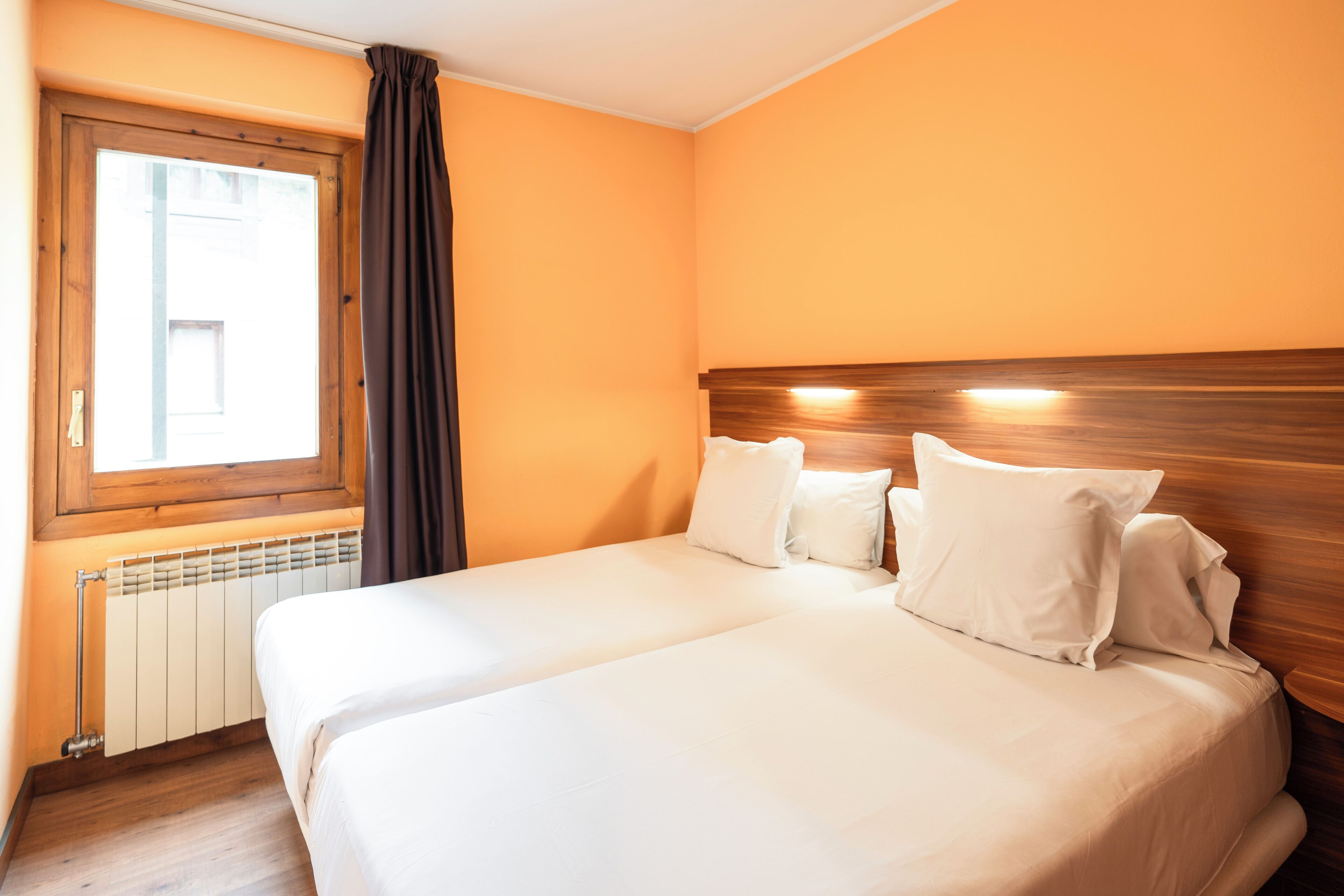 A hotel room with a large bed, a window with curtains, and a wooden headboard.