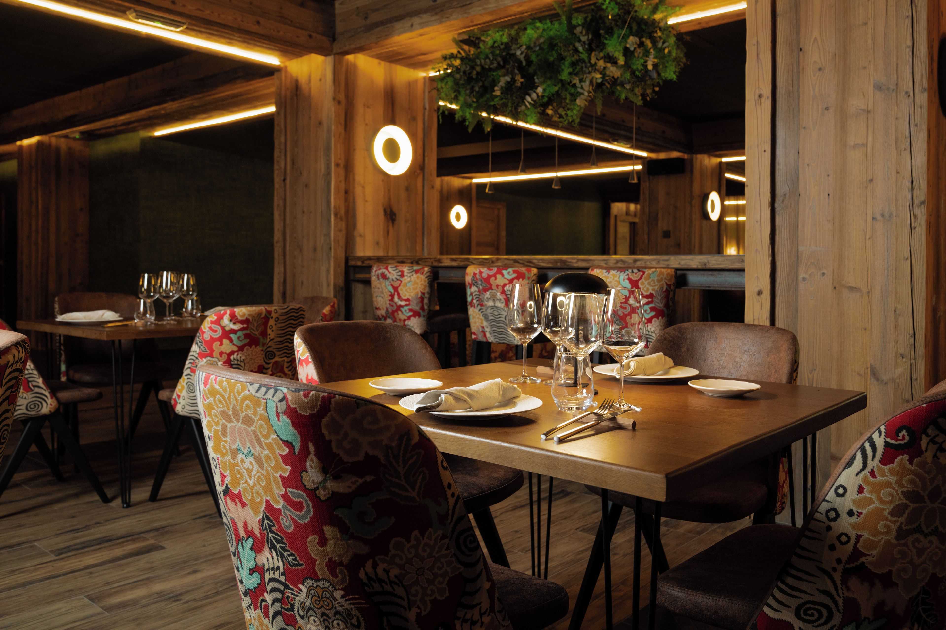 A dining area with a wooden table set for two, surrounded by patterned chairs.