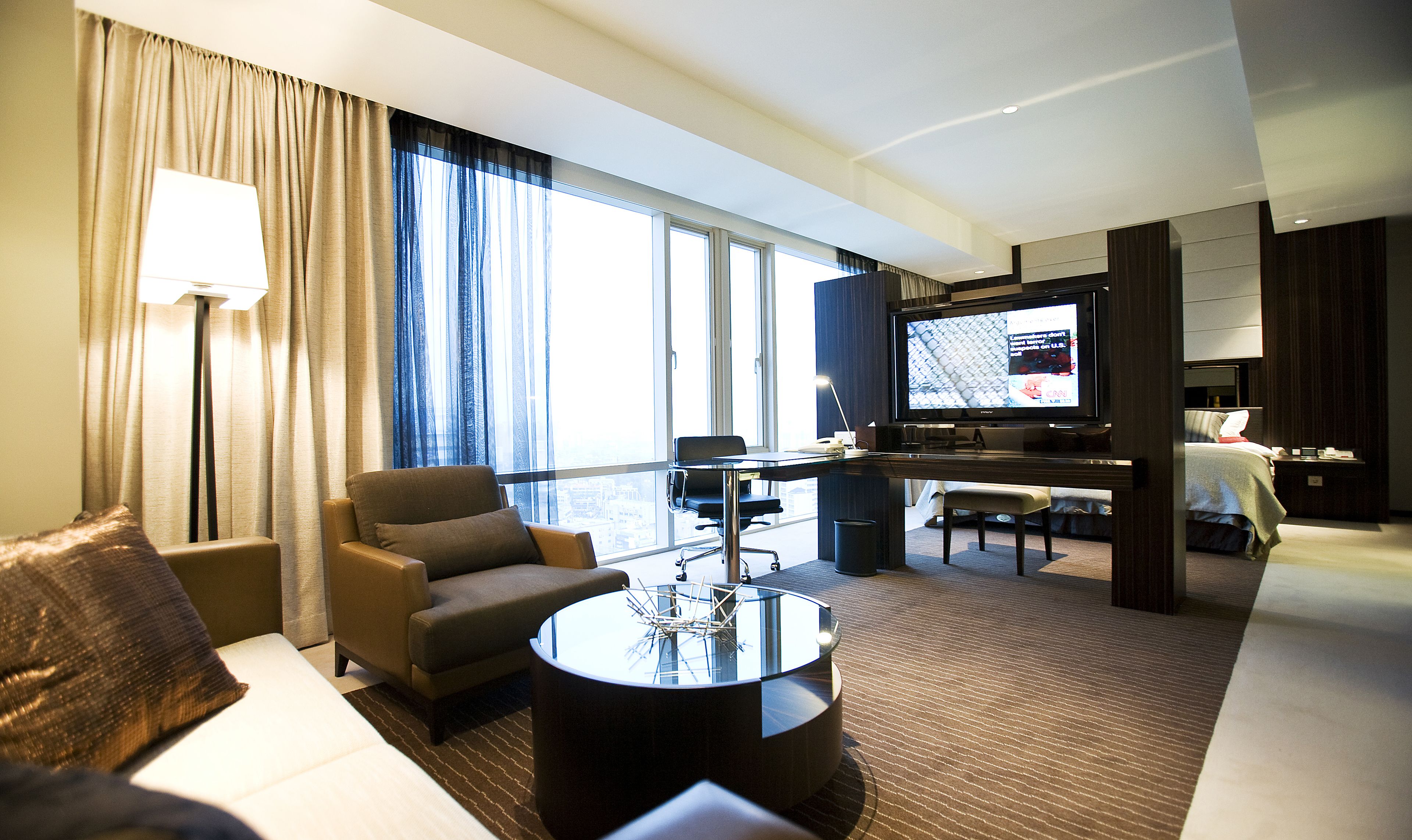 A hotel room with a living area featuring a sofa, armchair, coffee table, and a television.