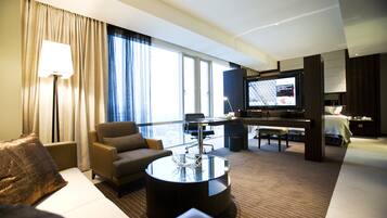 A hotel room with a living area featuring a sofa, armchair, coffee table, and a television.
