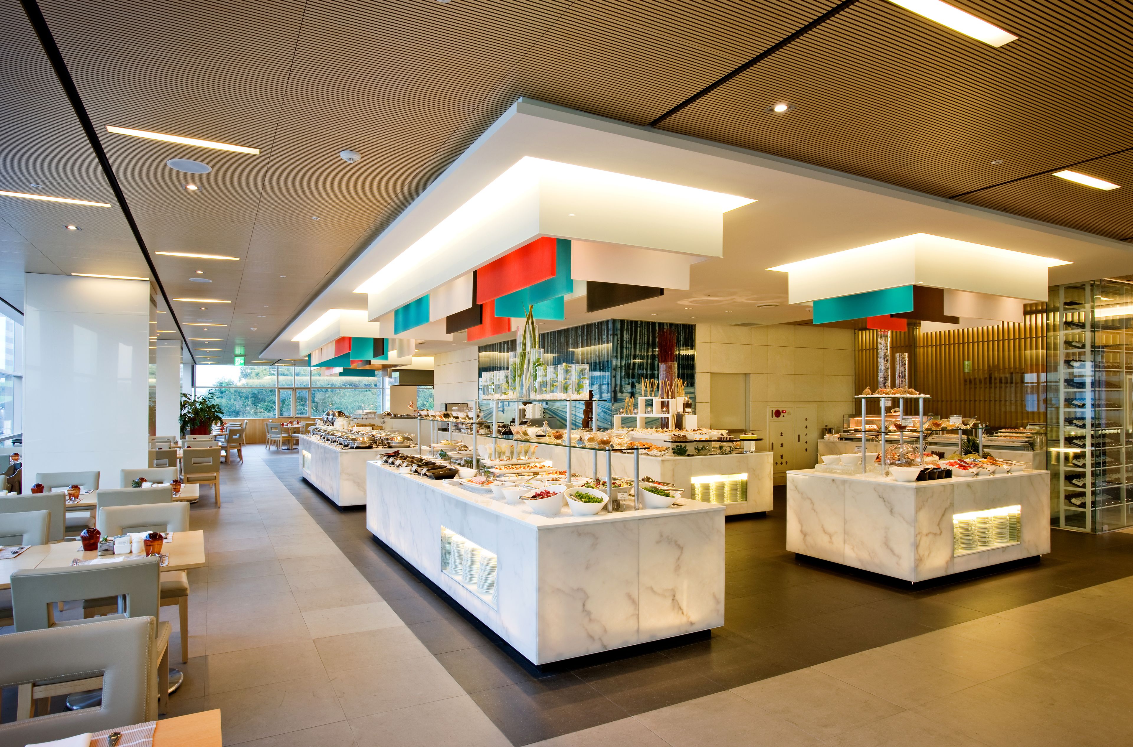 En moderne buffetopstilling med flere serveringsstationer, en indbydende og rummelig indretning samt udsigt til det fri gennem store vinduer.