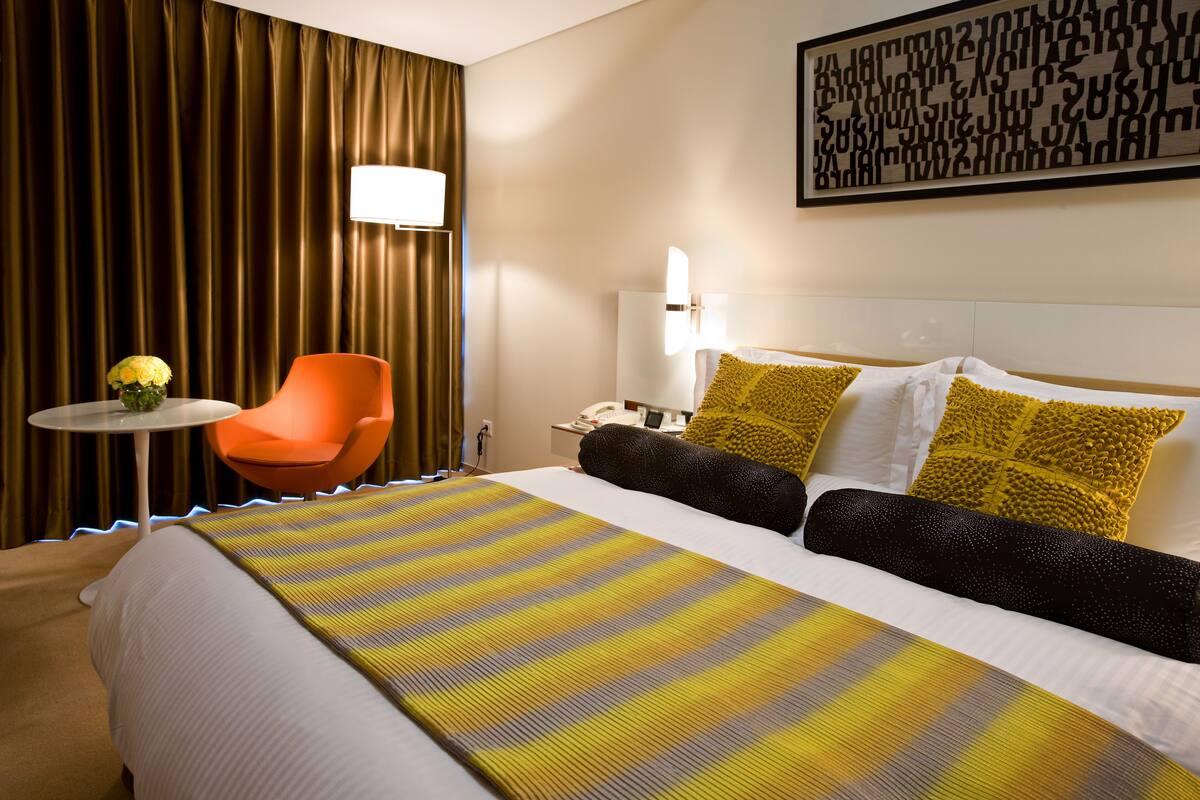 Habitación de hotel con una cama grande, una mesita pequeña, una silla anaranjada y una lámpara de pared.