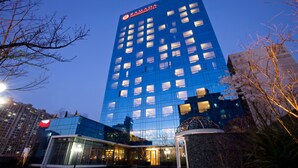 A modern hotel with a glass facade, multiple floors, and a prominent logo at the top. - Ramada Plaza Suwon (Suwon)