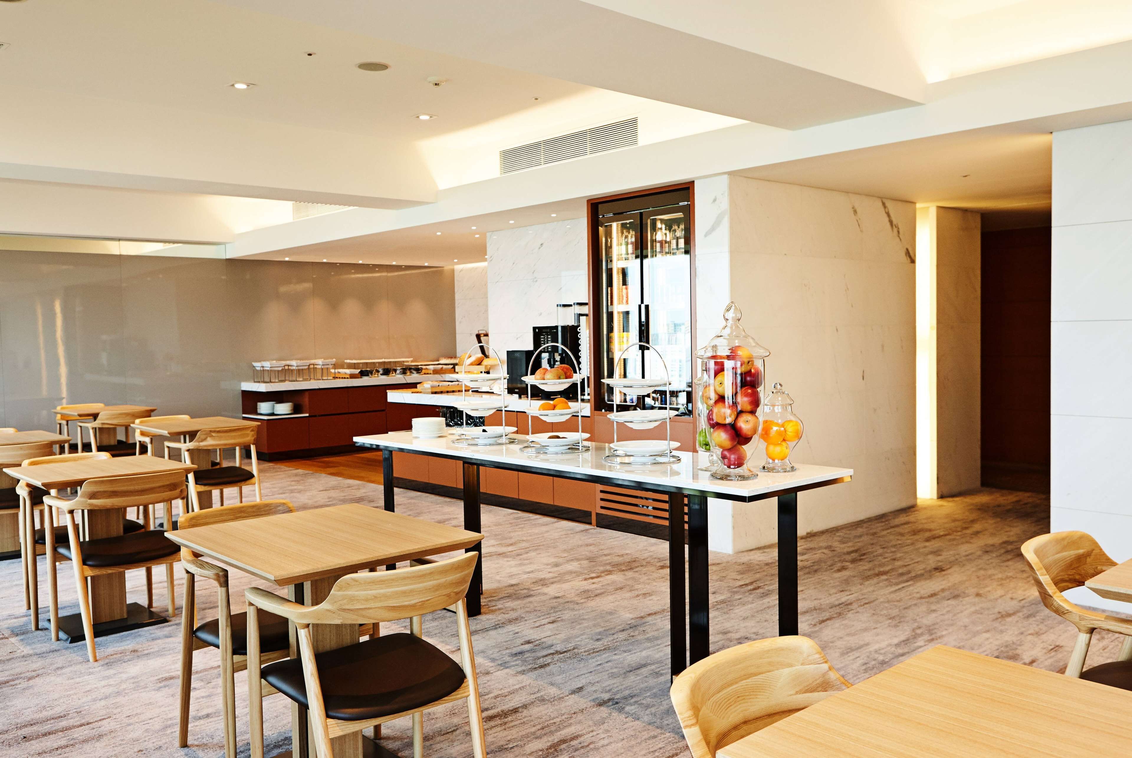 A modern dining area with wooden tables and chairs, a central serving station, and a large mirror reflecting the space.