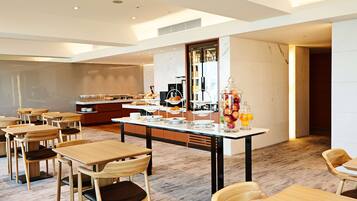 A modern dining area with wooden tables and chairs, a central serving station, and a large mirror reflecting the space.