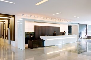 Un moderno espacio de recepción de hotel con mostrador, pantalla digital y cartel indicativo.
