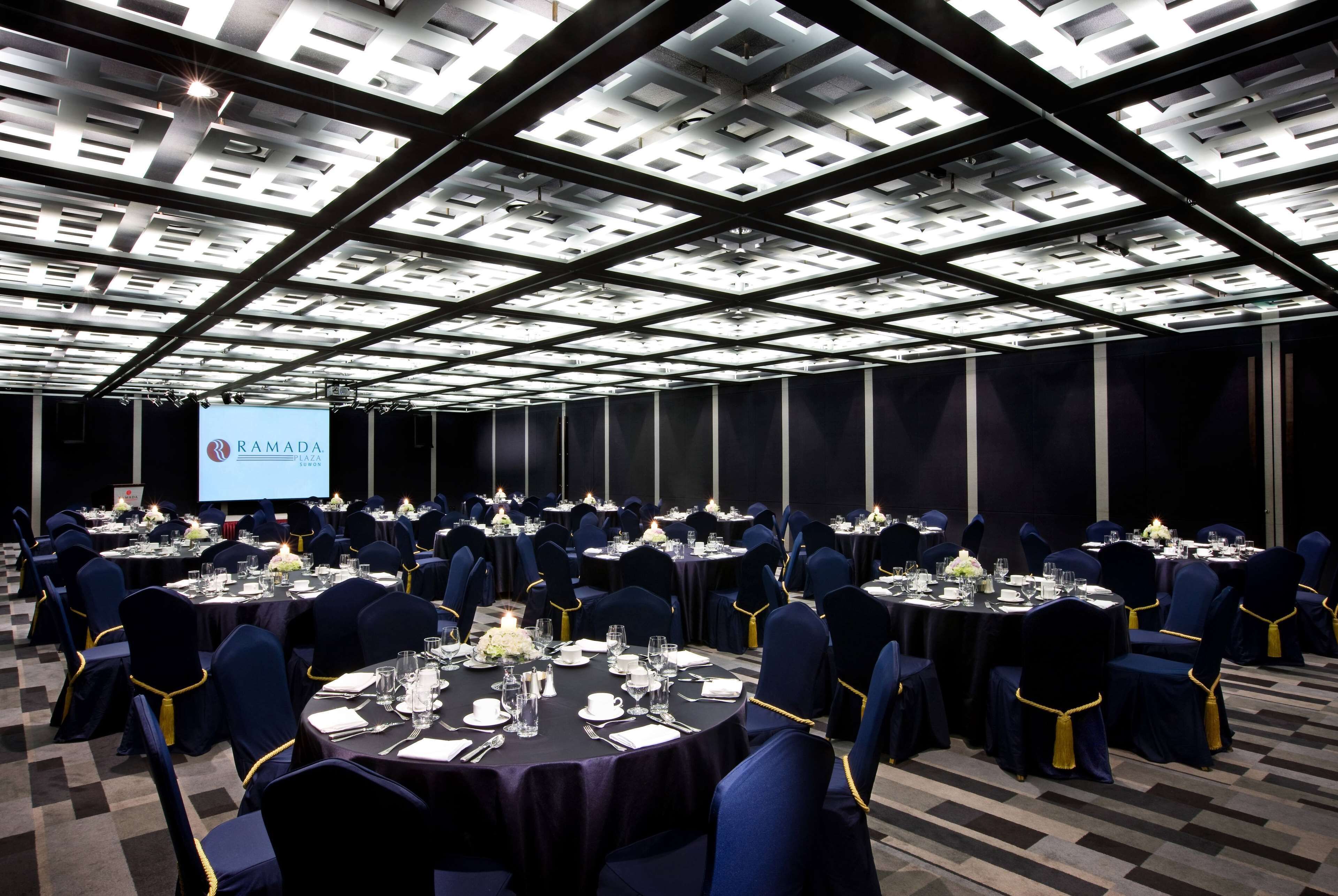 Un salón de conferencias con mesas redondas, sillas azul marino con detalles dorados y un techo con diseño geométrico.