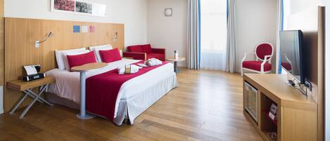 A hotel room with a bed, a desk, a chair, a TV, and a window with curtains.