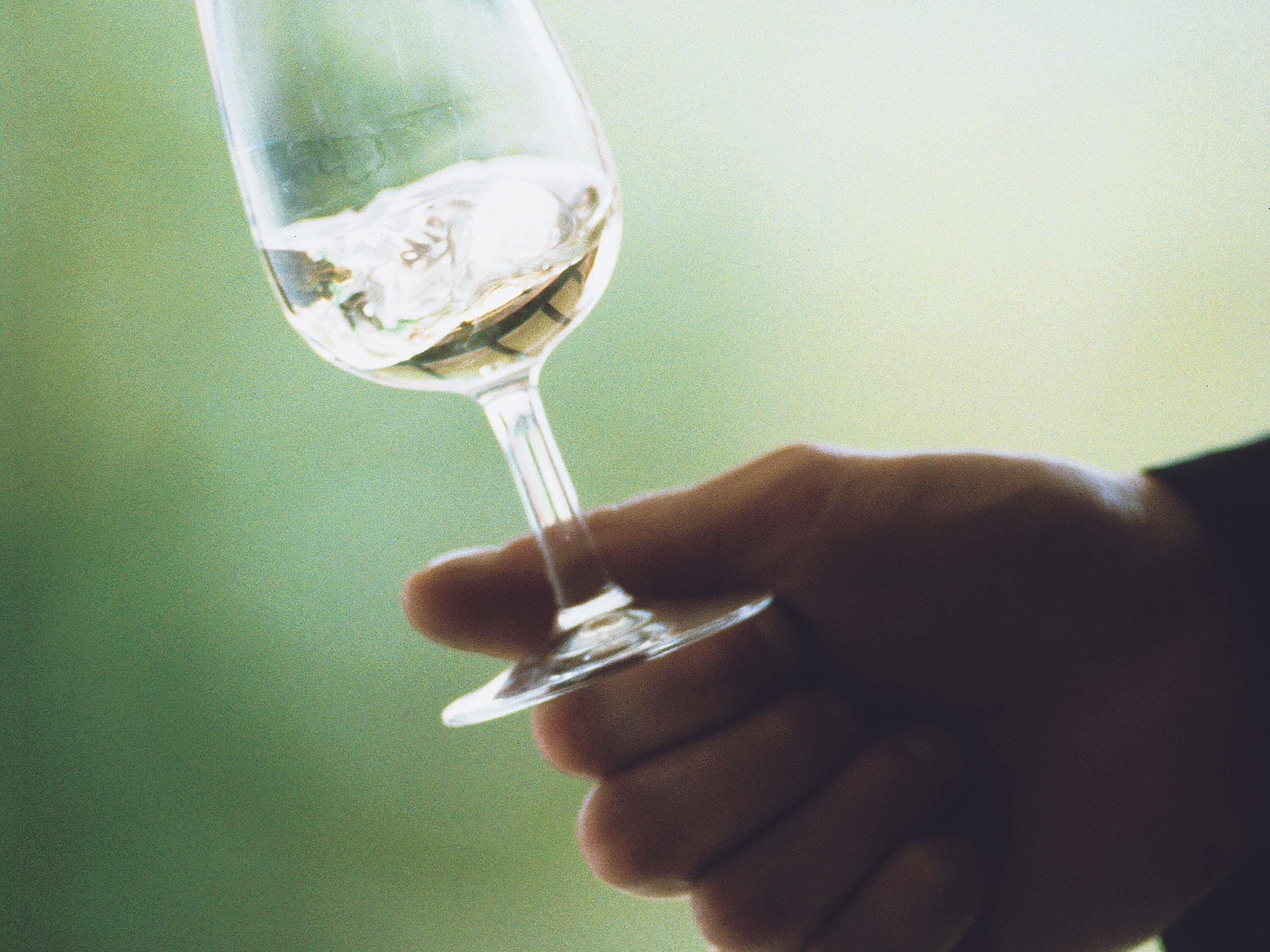A hand holding a clear glass with a liquid, possibly a drink, against a blurred background.