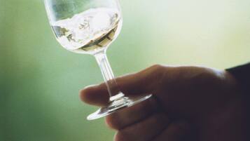 A hand holding a clear glass with a liquid, possibly a drink, against a blurred background.