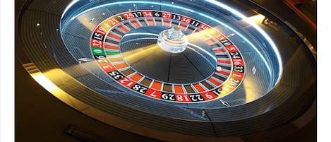 A roulette wheel with numbers and a ball in a casino setting.