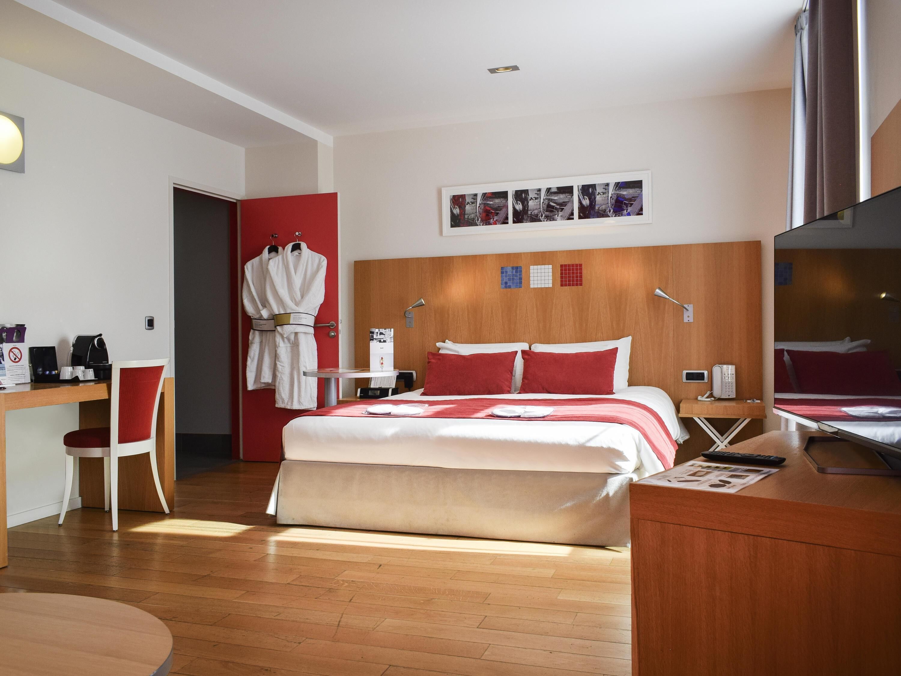 Una habitación de hotel con cama, escritorio, silla, perchero y espejo.