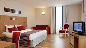 Una habitación de hotel con cama, escritorio, computadora, silla y televisor.