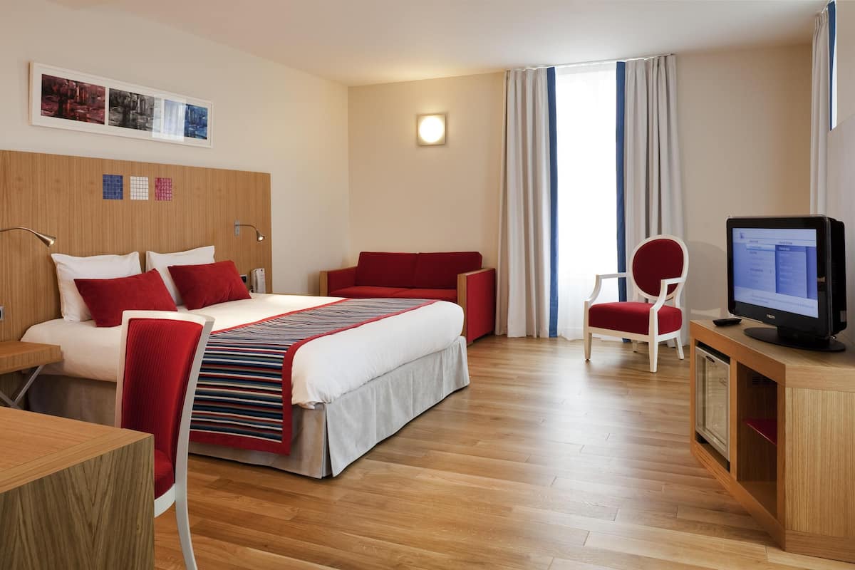 Una habitación de hotel con cama, escritorio, computadora, silla y televisor.