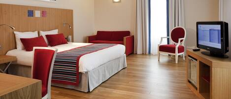 Una habitación de hotel con cama, escritorio, computadora, silla y televisor.