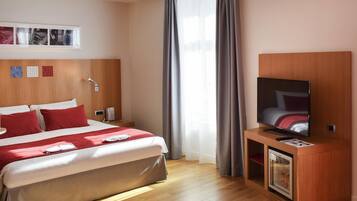 Een hotelkamer met een bed, een televisie, een minibar en een raam met gordijnen.