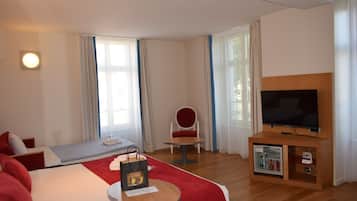A hotel room with a bed, a TV on a wooden stand, a small table with a chair, and a minibar.