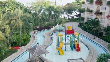 A pool area with multiple swimming pools, a children's play structure, and surrounding tropical vegetation.