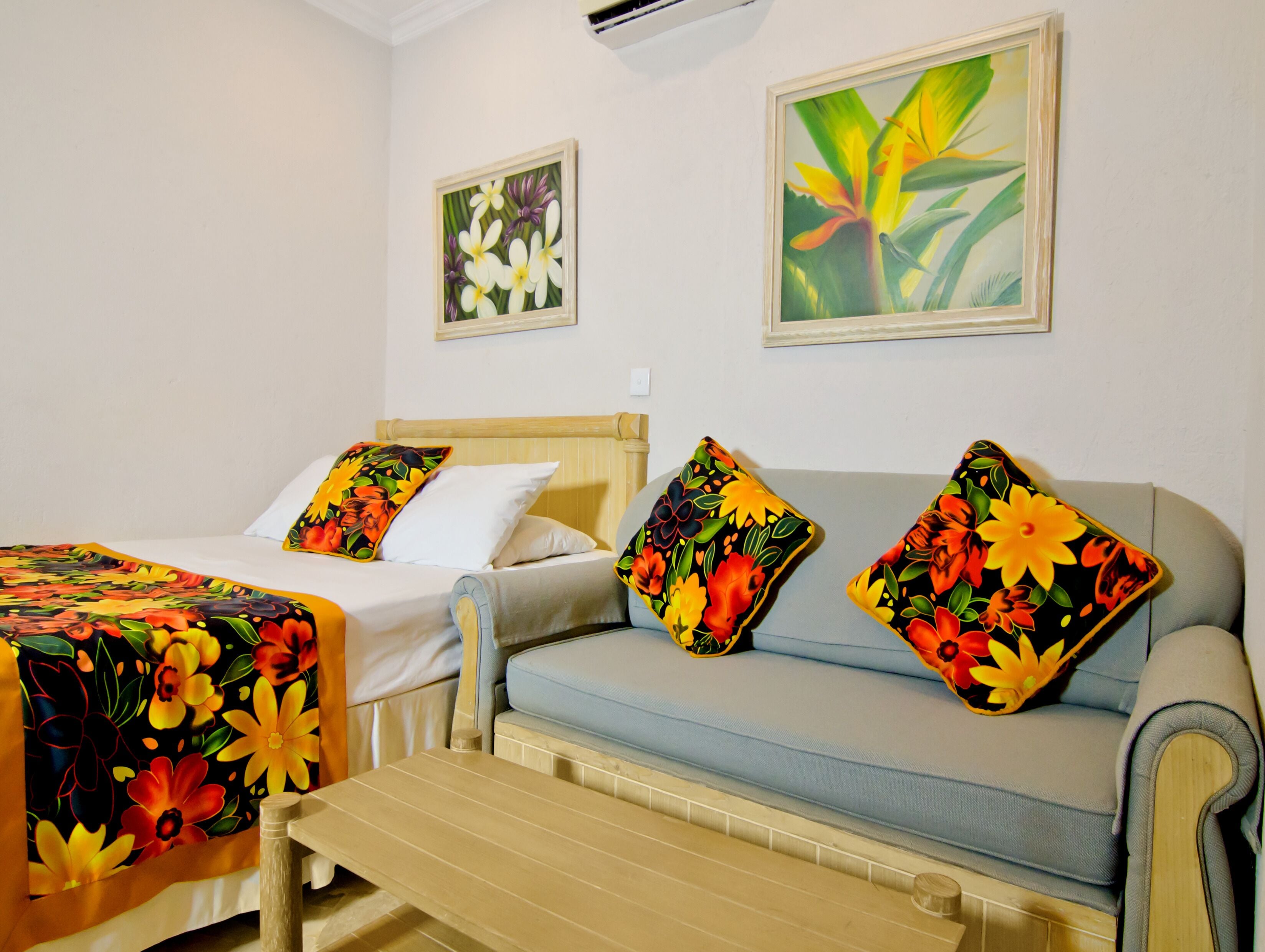 Una habitación de hotel con una cama, un sofá y un banco. Hay dos cuadros en las paredes.