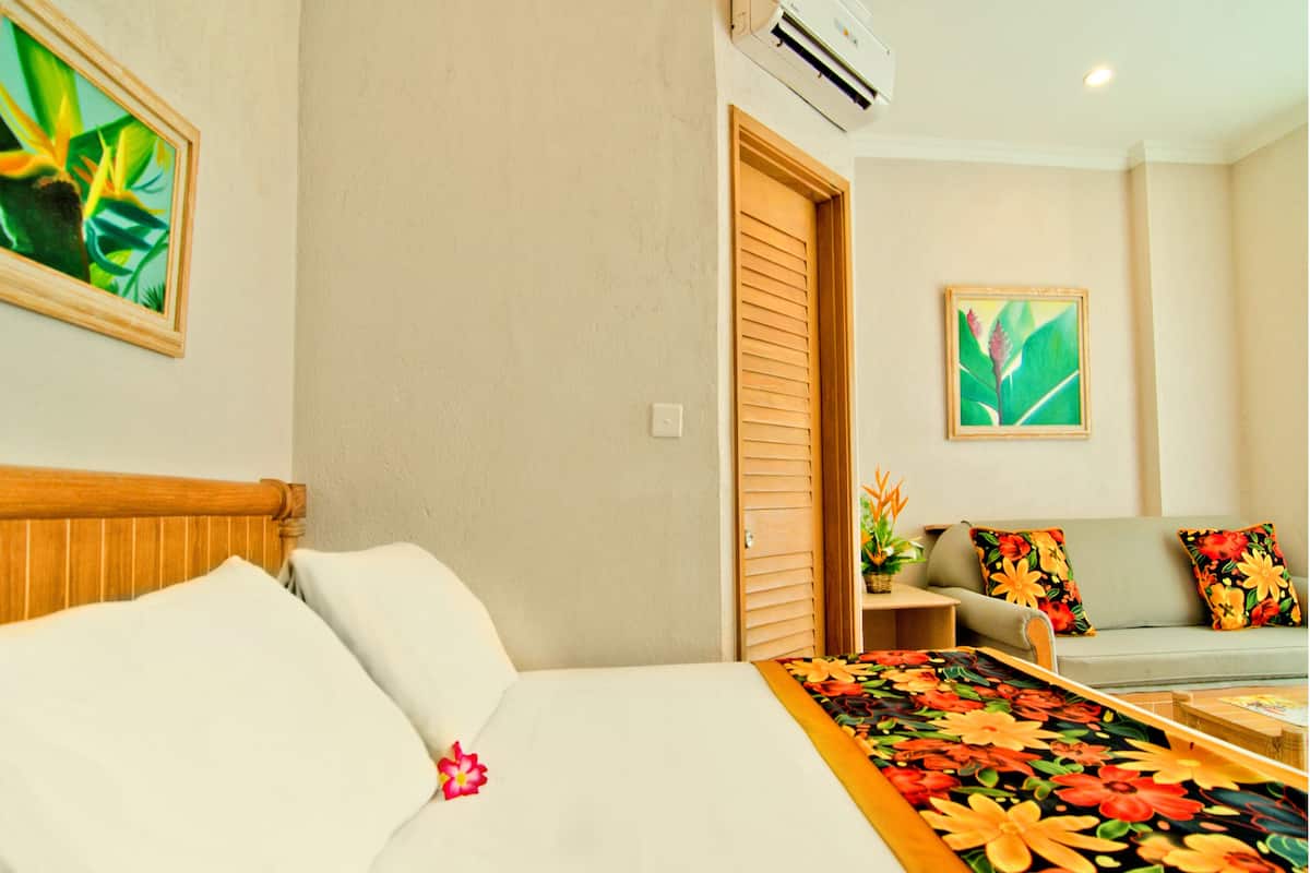 A hotel room with a bed, a sofa, a small table, and two paintings on the walls.