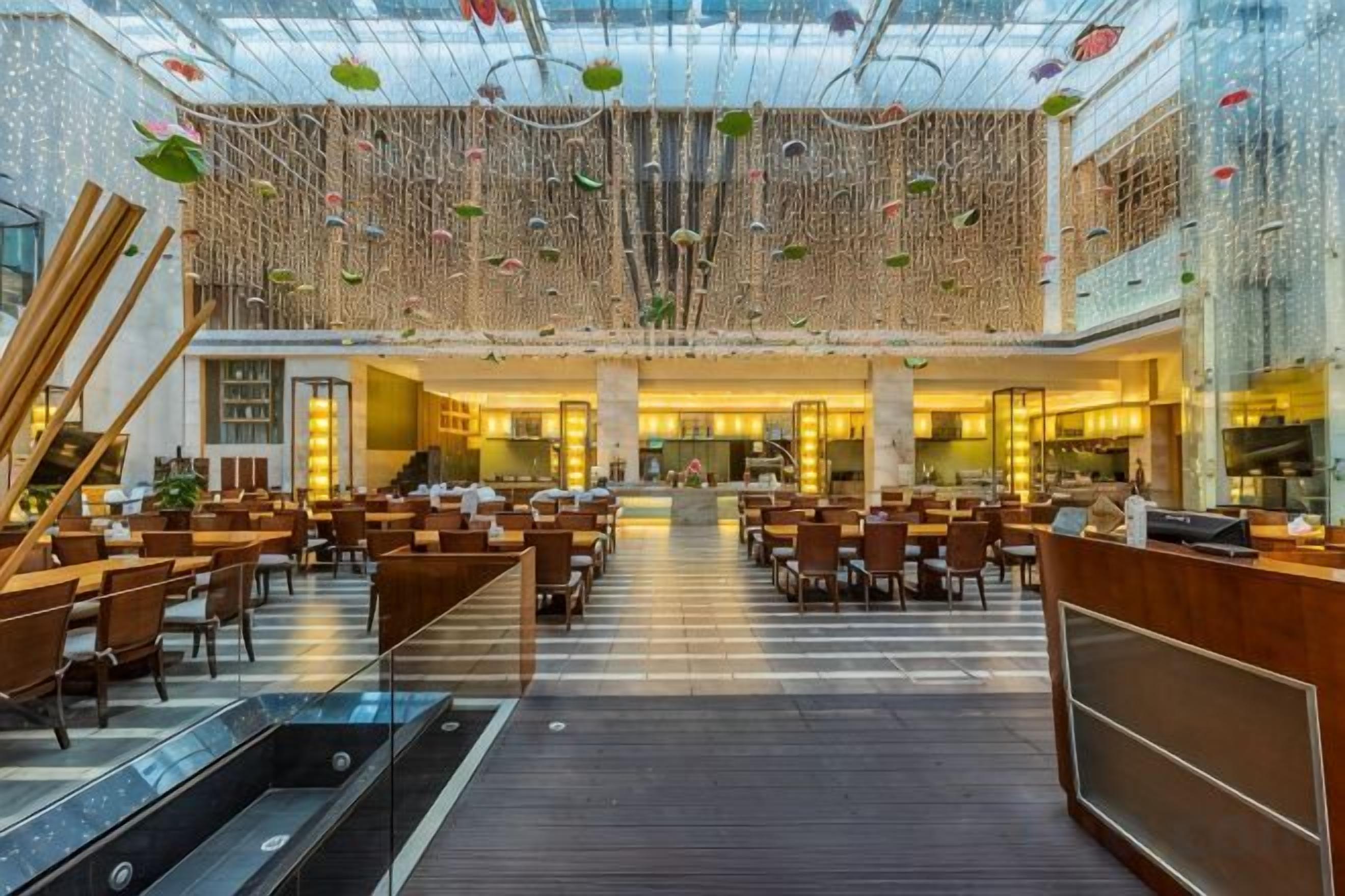 A spacious hotel lobby with a central staircase, multiple seating areas, and a high ceiling with hanging decorations.