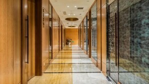 Un largo pasillo con paredes de madera, puertas de cristal y suelo de mármol.