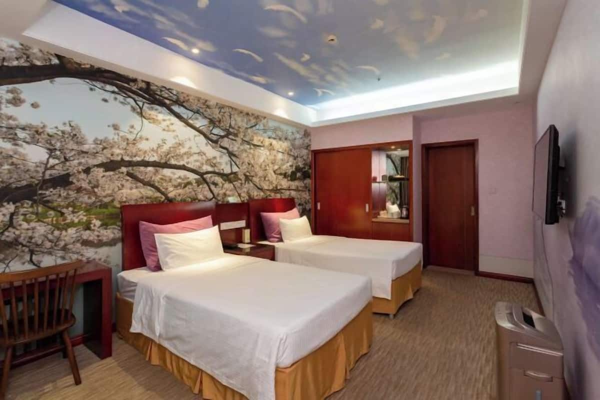 A hotel room with two beds, a ceiling mural, a desk, and a television.