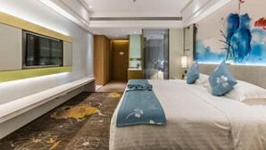 Una habitación de hotel con cama, televisión, baño y un cuadro en la pared.