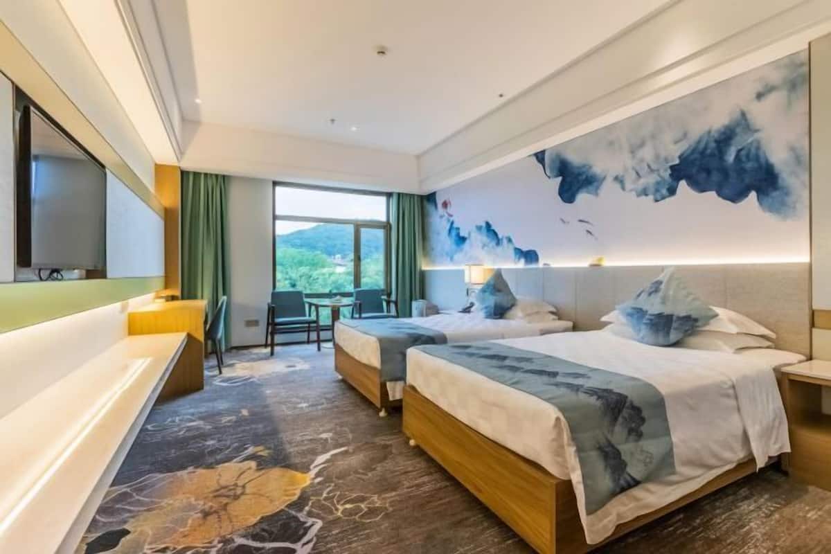 A hotel room with two beds, a desk, a chair, a TV, and a large window with a view.