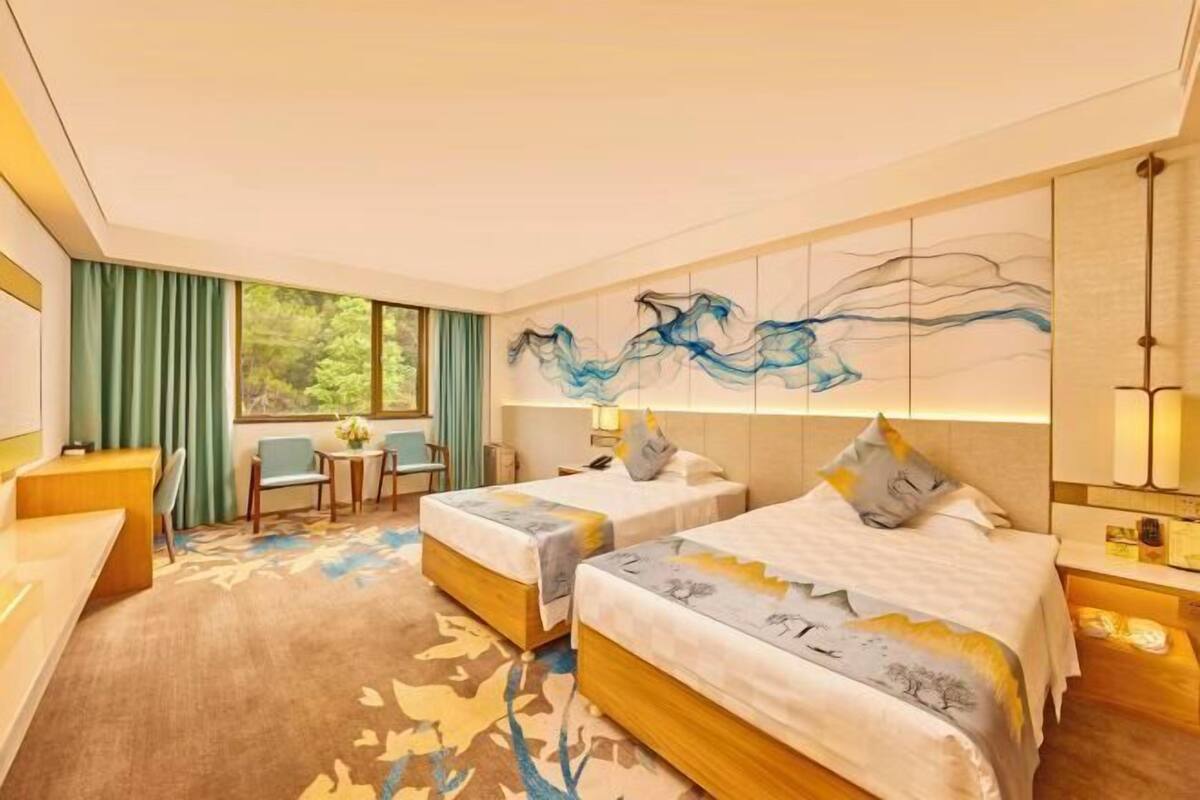 A hotel room with two beds, a desk, a chair, a window with curtains, and a wall art piece.