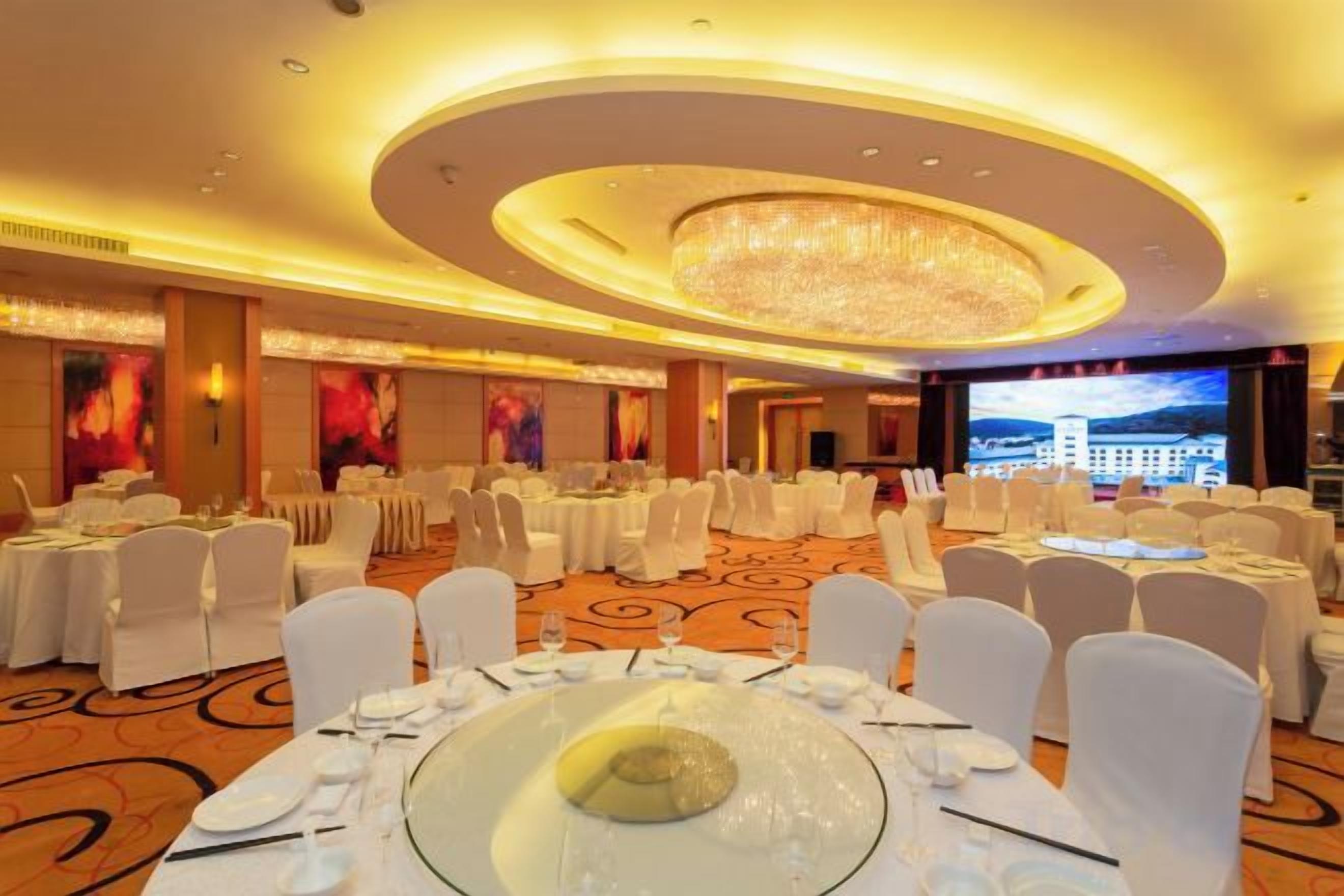 A banquet hall with round tables, white chairs, and a large chandelier.