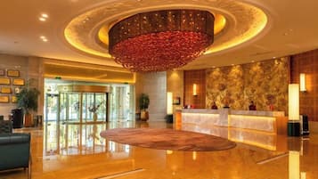 A hotel lobby with a reception desk, a large circular carpet, and a decorative ceiling light fixture.
