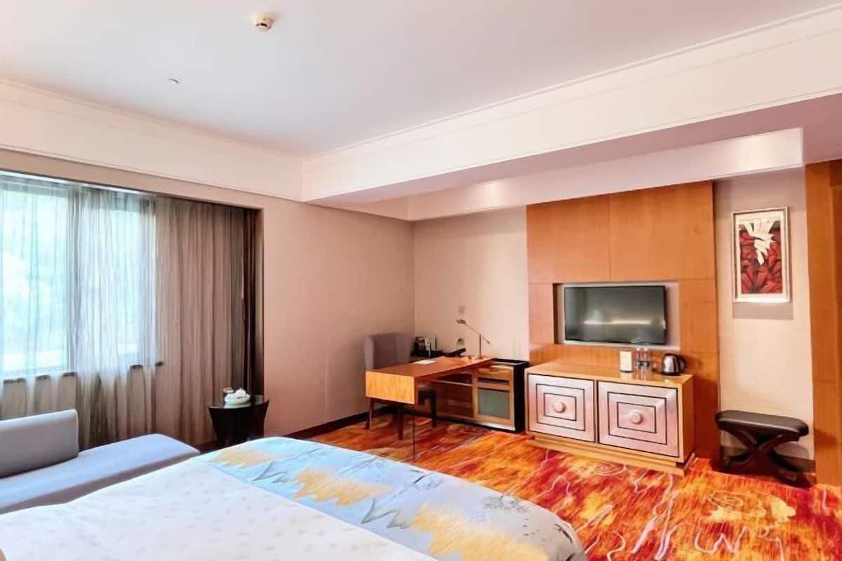 A hotel room with a bed, a desk, a television, and a cabinet.